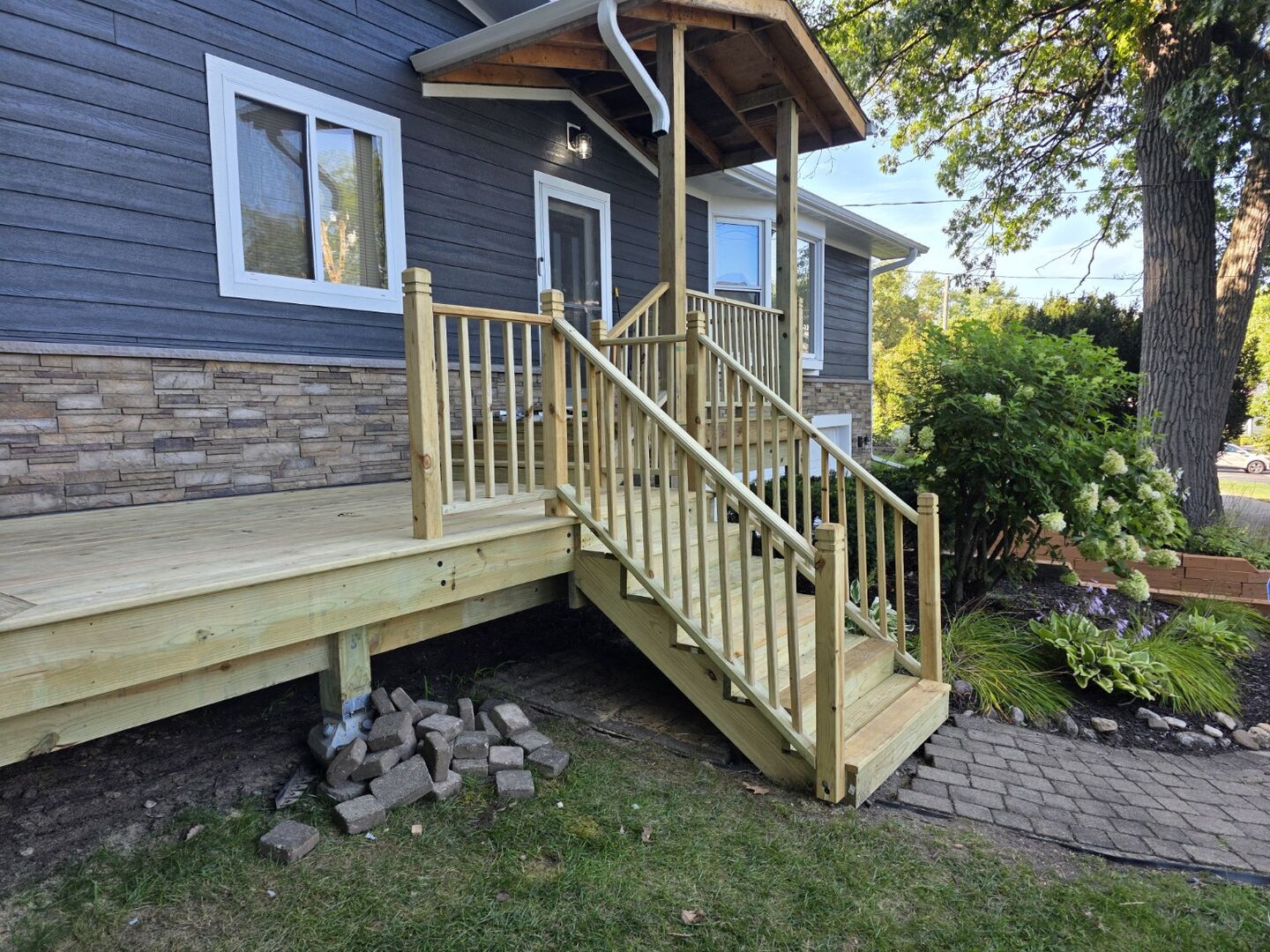 Completed wood deck with new stairs and railing beside a home