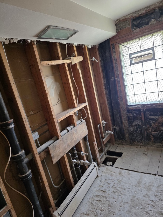 Bathroom stripped to the studs with plumbing exposed